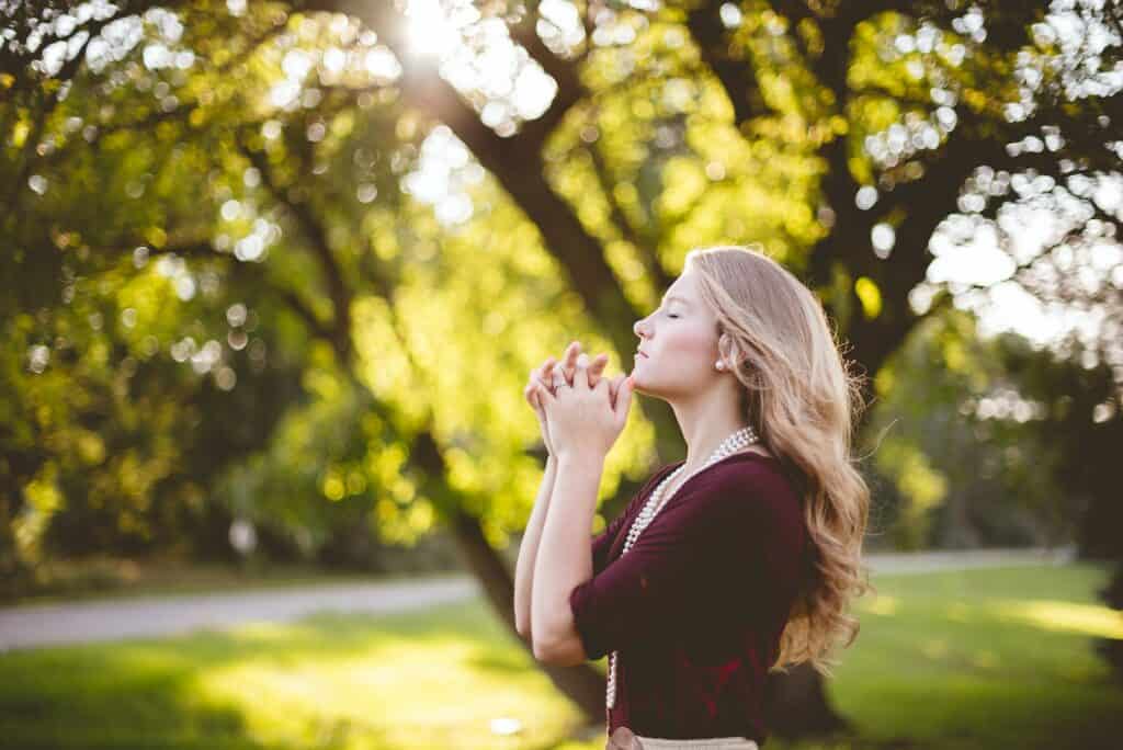 is manifesting and praying the same thing? woman praying under tree during daytime